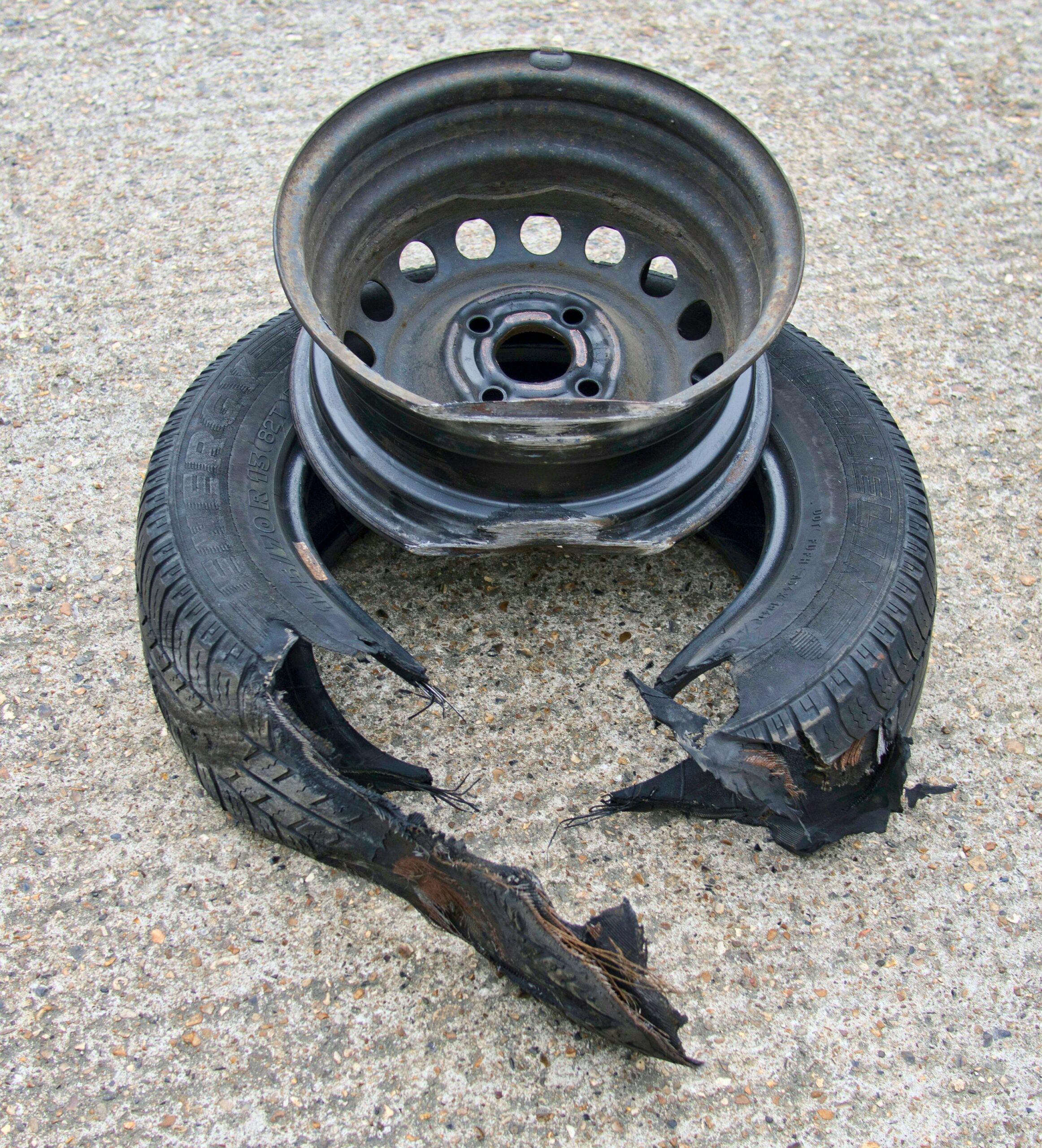 Detailed shot of a damaged car wheel and tire on a concrete surface.