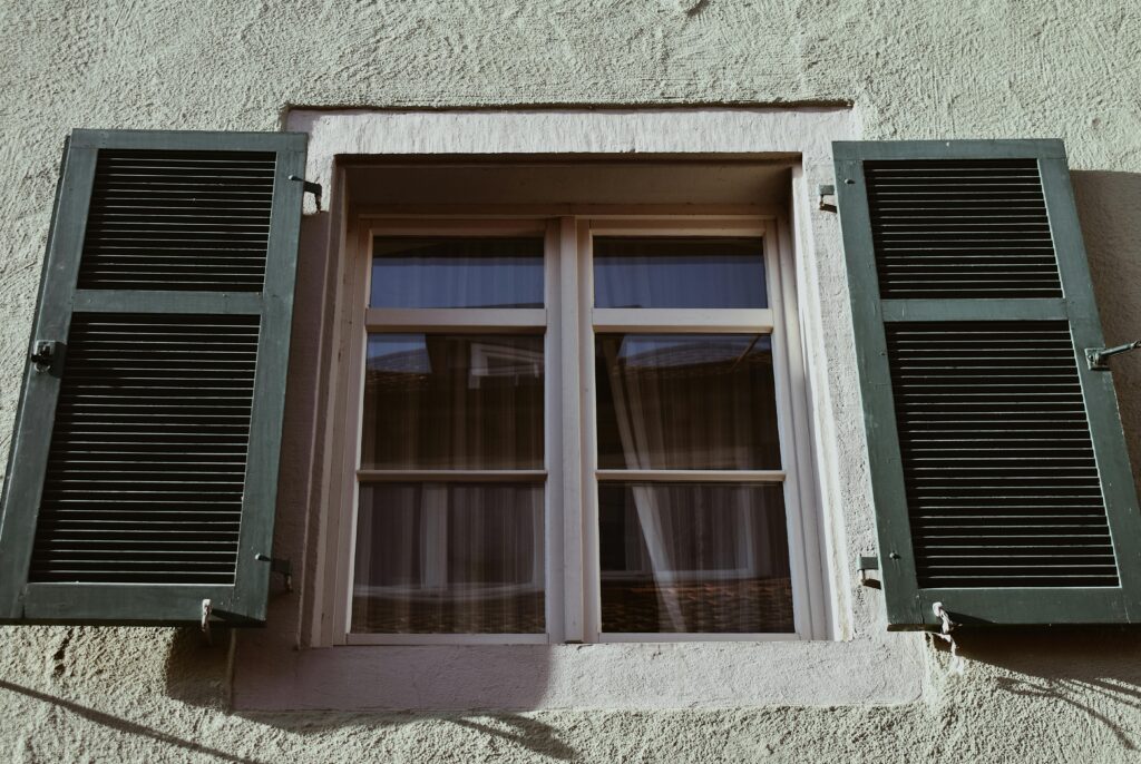 Close-up of a classic window with open green shutters on an aged stucco wall.